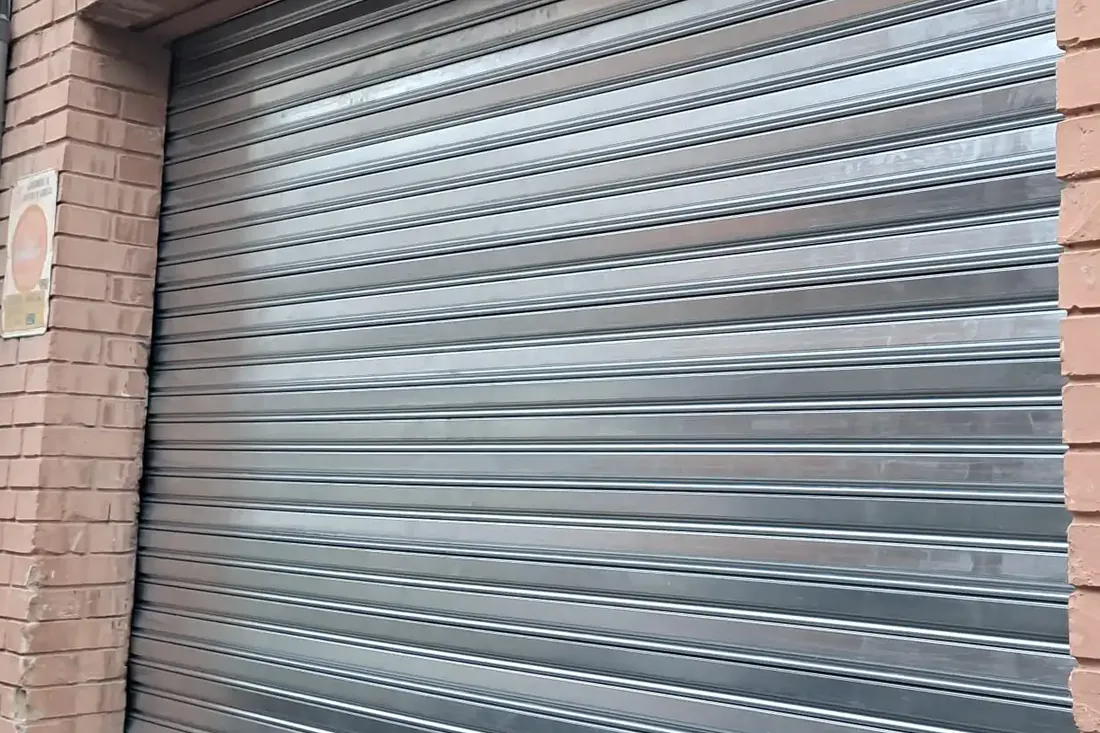 Persiana metalica bajada en la fachada de ladrillo de un local